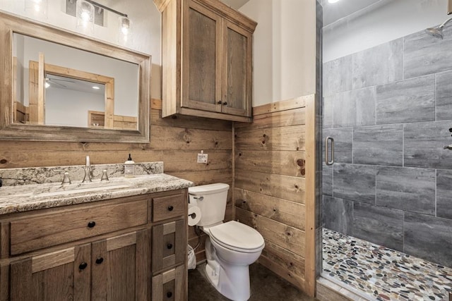 bathroom with vanity, toilet, a shower with door, and wooden walls