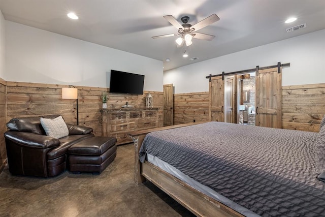 bedroom featuring wood walls, ceiling fan, and a barn door