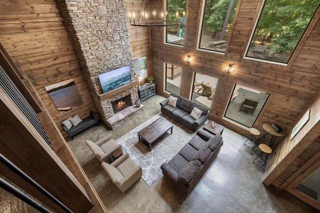 living room with high vaulted ceiling, wooden walls, a fireplace, concrete floors, and a notable chandelier