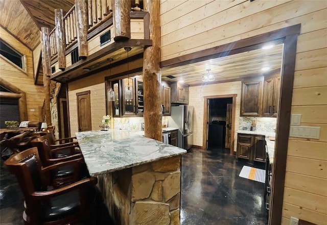 interior space with light stone countertops, stainless steel refrigerator with ice dispenser, wood walls, a kitchen bar, and decorative backsplash