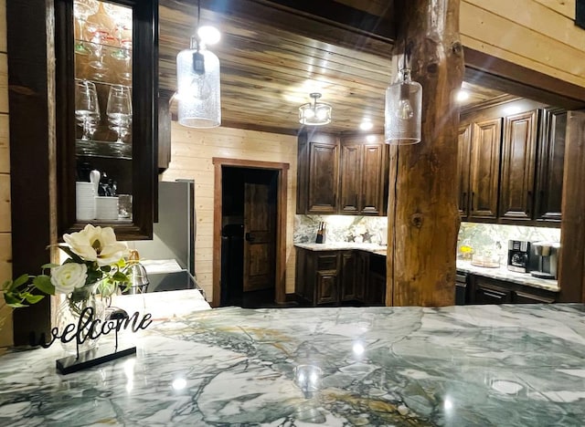 kitchen featuring pendant lighting, wood walls, light stone counters, and dark brown cabinetry