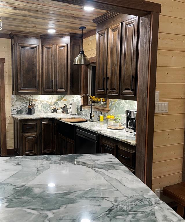 kitchen with pendant lighting, dark brown cabinetry, light stone counters, and wooden walls