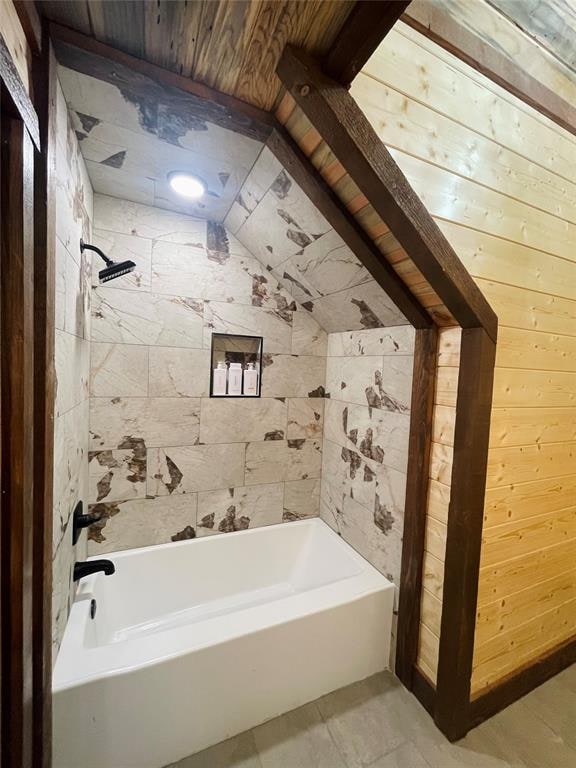 bathroom featuring tile patterned flooring, tiled shower / bath, wooden walls, and vaulted ceiling