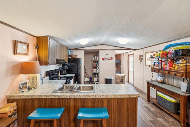 kitchen featuring black appliances, a kitchen breakfast bar, vaulted ceiling, dark hardwood / wood-style floors, and kitchen peninsula