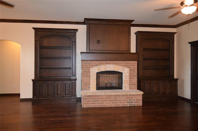 unfurnished living room featuring crown molding, dark hardwood / wood-style flooring, ceiling fan, and a brick fireplace