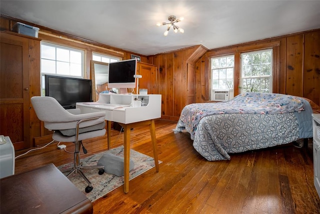 bedroom featuring multiple windows, wood walls, hardwood / wood-style floors, and cooling unit