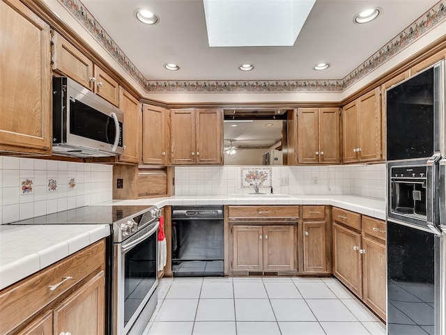 kitchen with appliances with stainless steel finishes, backsplash, a skylight, sink, and tile countertops