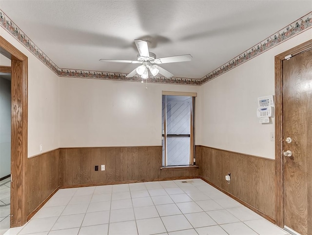 unfurnished room with a textured ceiling, ceiling fan, and wood walls