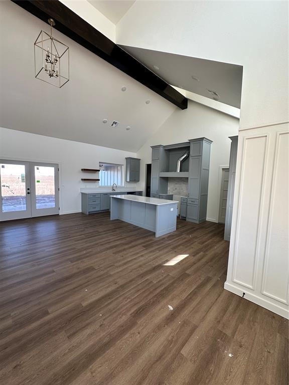 unfurnished living room featuring high vaulted ceiling, a notable chandelier, dark wood-type flooring, beam ceiling, and french doors