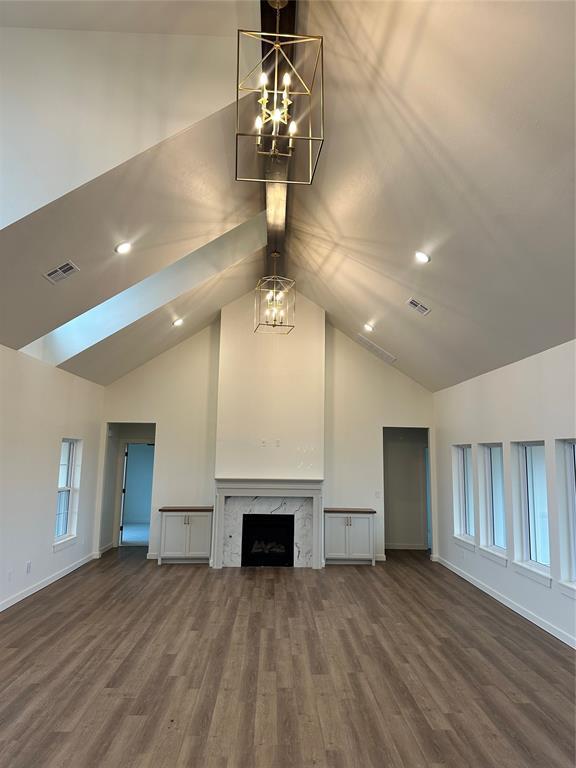 unfurnished living room featuring an inviting chandelier, hardwood / wood-style flooring, high vaulted ceiling, and a premium fireplace