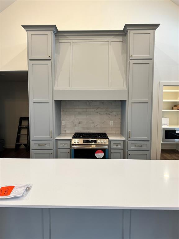 kitchen featuring lofted ceiling, gray cabinets, gas stove, and custom exhaust hood