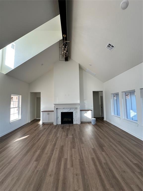 unfurnished living room with an inviting chandelier, a high end fireplace, high vaulted ceiling, and dark hardwood / wood-style floors