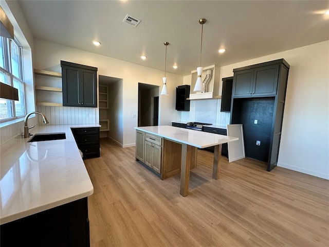 kitchen with pendant lighting, a center island, sink, light wood-type flooring, and light stone countertops