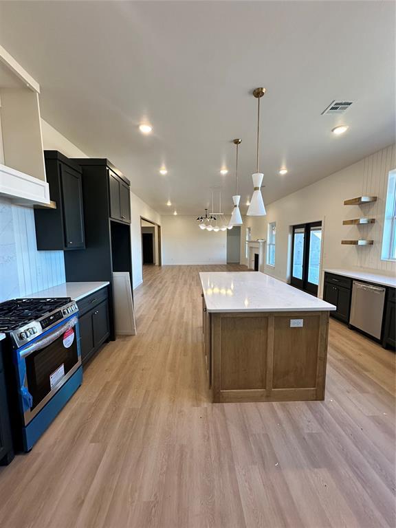 kitchen with a center island, light wood-type flooring, stainless steel appliances, and hanging light fixtures