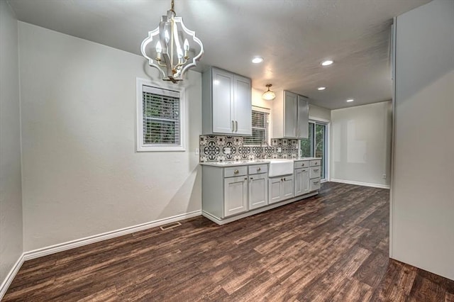 kitchen with backsplash, an inviting chandelier, hanging light fixtures, gray cabinets, and dark hardwood / wood-style flooring