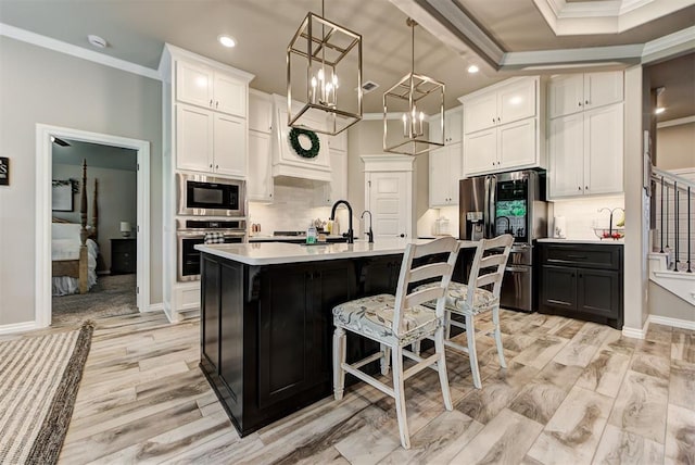 kitchen featuring a kitchen island with sink, white cabinets, stainless steel appliances, and decorative light fixtures