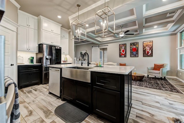 kitchen with stainless steel appliances, coffered ceiling, a barn door, a kitchen island with sink, and white cabinets