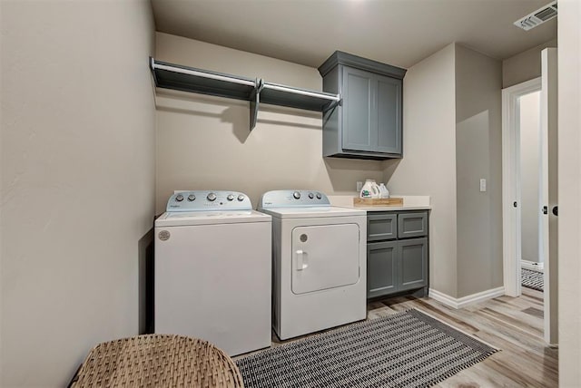 clothes washing area featuring cabinets, light wood-type flooring, and washing machine and clothes dryer