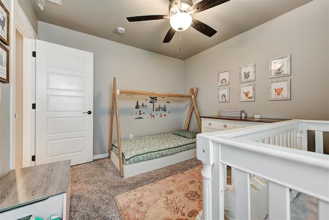 carpeted bedroom with ceiling fan and a nursery area