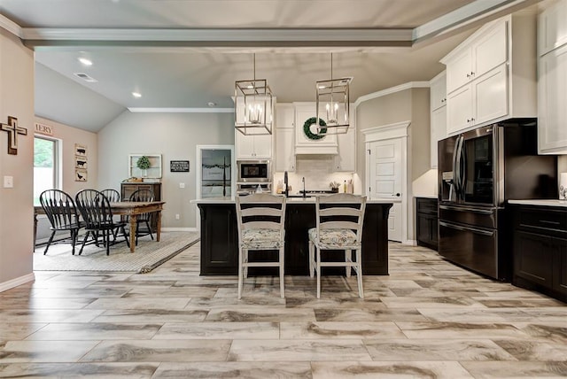 kitchen with crown molding, decorative light fixtures, a kitchen island with sink, white cabinets, and appliances with stainless steel finishes