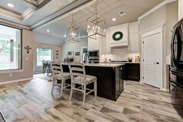 kitchen featuring a kitchen island with sink, white cabinets, crown molding, decorative light fixtures, and stainless steel appliances