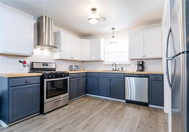 kitchen with wall chimney exhaust hood, hanging light fixtures, stainless steel appliances, wood counters, and white cabinets