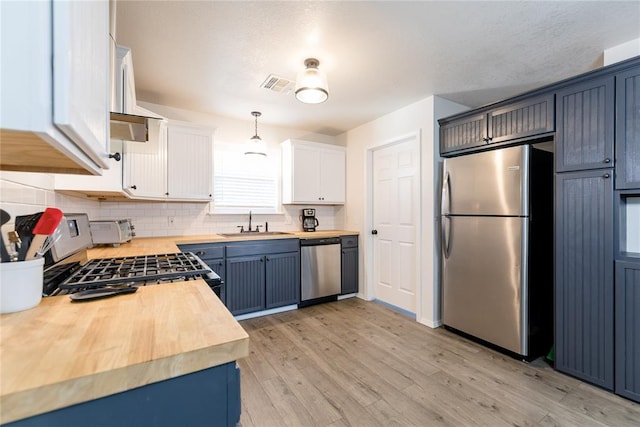 kitchen with white cabinetry, light hardwood / wood-style flooring, butcher block countertops, decorative light fixtures, and appliances with stainless steel finishes