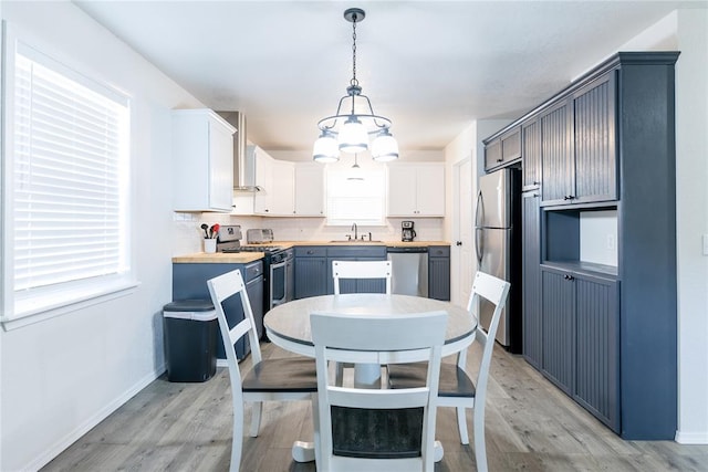 kitchen with wood counters, stainless steel appliances, white cabinets, light hardwood / wood-style floors, and hanging light fixtures