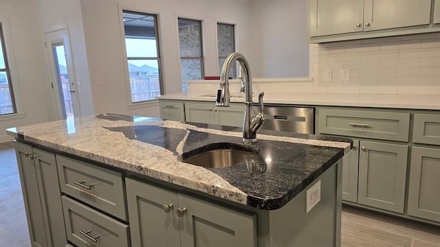 kitchen with dishwasher, tasteful backsplash, light stone countertops, an island with sink, and light wood-type flooring