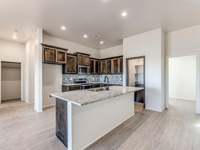 kitchen featuring sink, light stone counters, a kitchen island with sink, appliances with stainless steel finishes, and light wood-type flooring