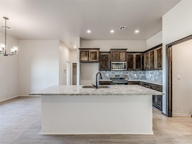 kitchen featuring light stone counters, stainless steel appliances, sink, pendant lighting, and a center island with sink