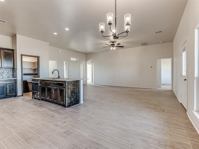 kitchen featuring dark brown cabinetry, tasteful backsplash, an island with sink, pendant lighting, and ceiling fan with notable chandelier