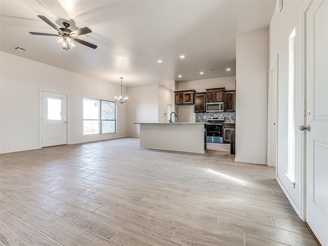 unfurnished living room featuring ceiling fan with notable chandelier and light hardwood / wood-style flooring