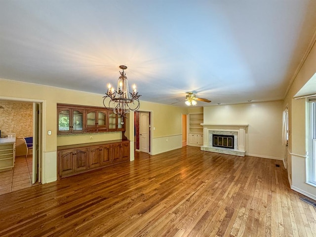 unfurnished living room featuring hardwood / wood-style flooring, ceiling fan with notable chandelier, a healthy amount of sunlight, and crown molding