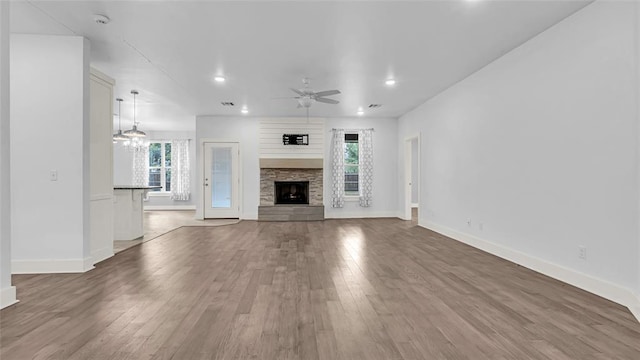 unfurnished living room with a stone fireplace, wood-type flooring, and ceiling fan with notable chandelier