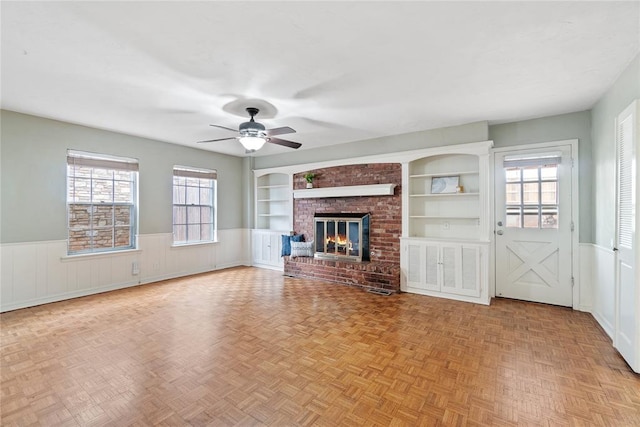 unfurnished living room featuring a fireplace, built in features, a wealth of natural light, and ceiling fan