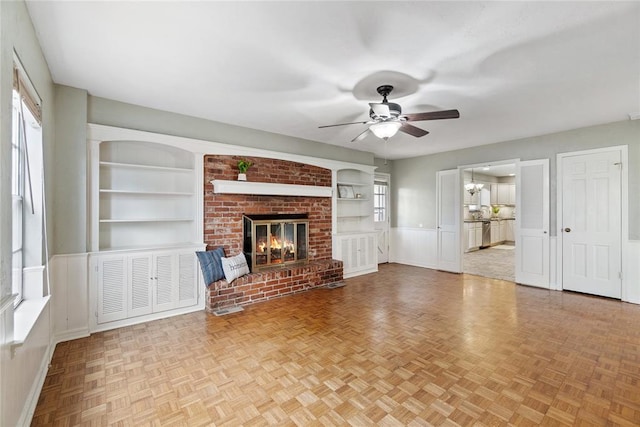 unfurnished living room featuring a fireplace, a wealth of natural light, built in features, and ceiling fan with notable chandelier