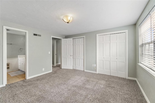 unfurnished bedroom featuring carpet, connected bathroom, and two closets