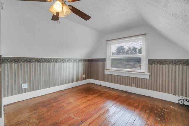 additional living space featuring ceiling fan, wood-type flooring, a textured ceiling, vaulted ceiling, and wooden walls