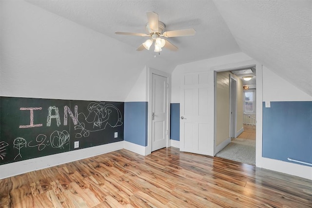 additional living space featuring a textured ceiling, ceiling fan, lofted ceiling, and light wood-type flooring