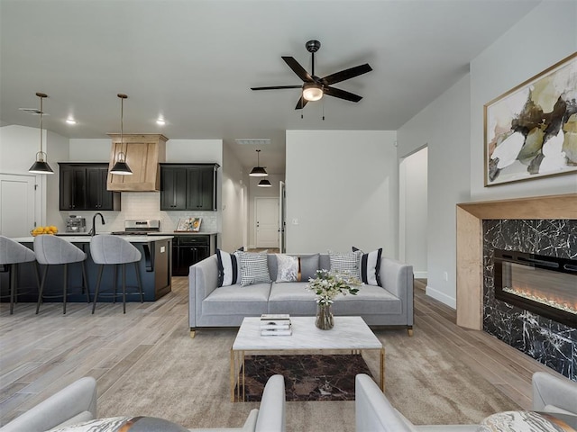 living room featuring ceiling fan, sink, light wood-type flooring, and a fireplace