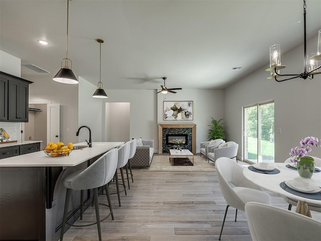 kitchen featuring a high end fireplace, ceiling fan with notable chandelier, sink, hanging light fixtures, and light hardwood / wood-style flooring