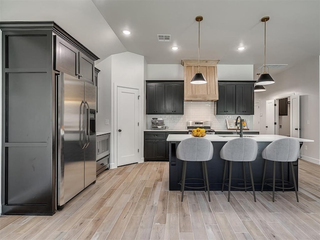 kitchen with pendant lighting, stainless steel appliances, a kitchen island with sink, and light hardwood / wood-style floors