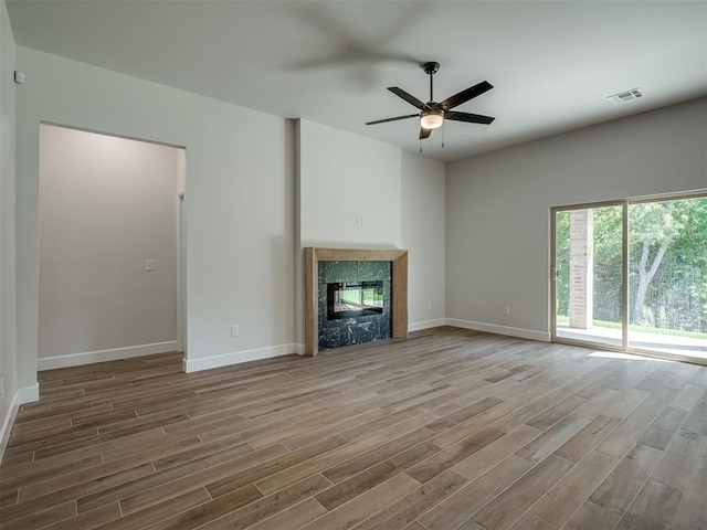 unfurnished living room with a high end fireplace, hardwood / wood-style flooring, and ceiling fan