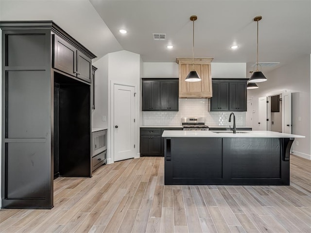 kitchen with sink, a kitchen island with sink, stainless steel appliances, decorative backsplash, and light wood-type flooring