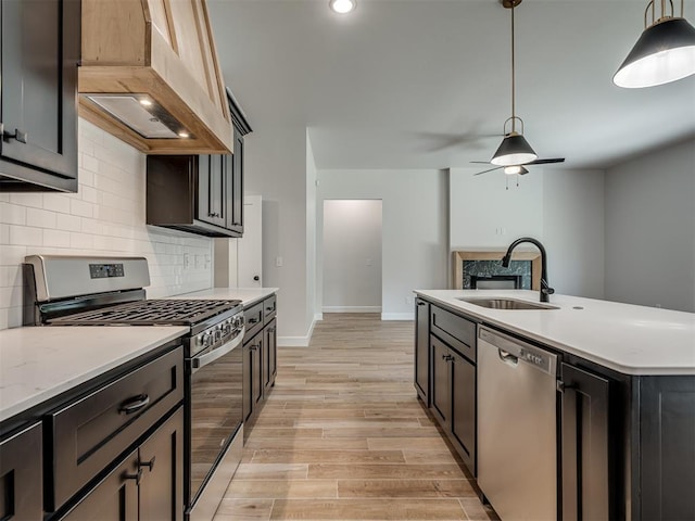 kitchen with appliances with stainless steel finishes, premium range hood, sink, light hardwood / wood-style floors, and hanging light fixtures