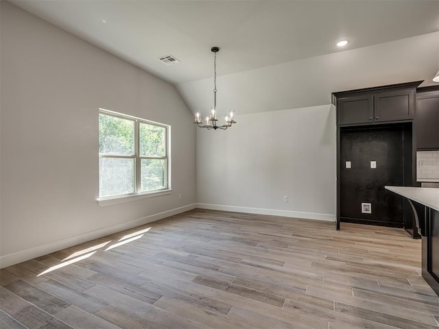 unfurnished dining area with light hardwood / wood-style floors, vaulted ceiling, and a notable chandelier