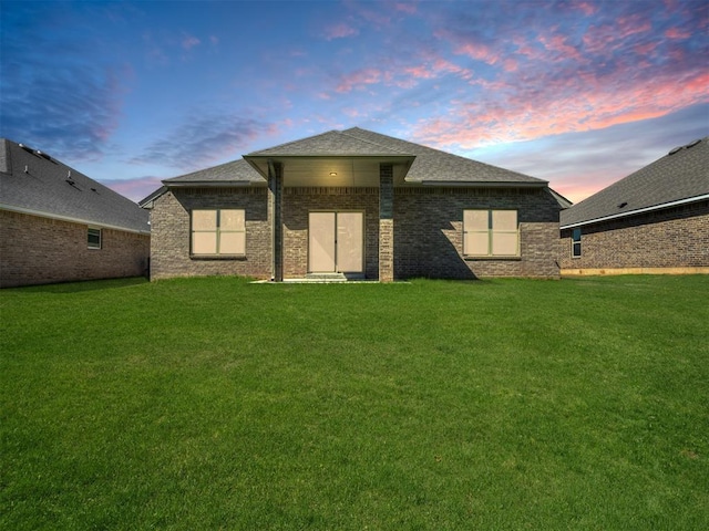 back house at dusk featuring a lawn