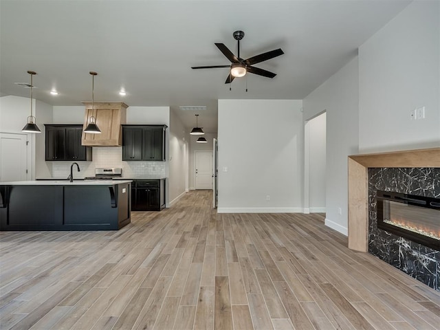 kitchen featuring a fireplace, decorative light fixtures, light wood-type flooring, and an island with sink