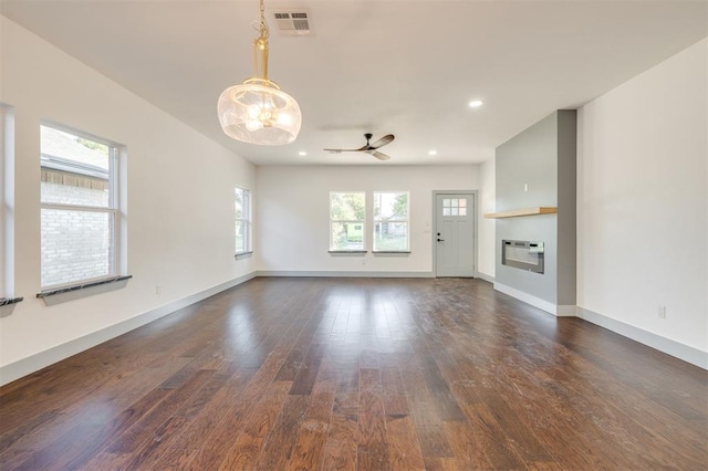 unfurnished living room featuring plenty of natural light, dark hardwood / wood-style floors, ceiling fan, and heating unit